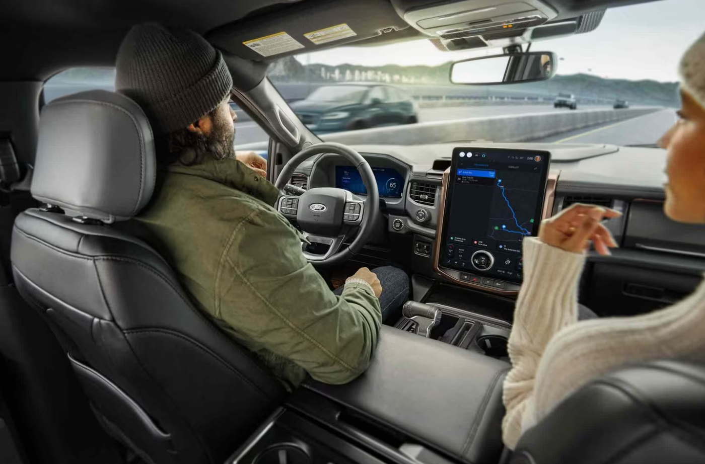 A man sits in the driver's seat of a Ford showing the infotainment system, dash, and safety systems available to him